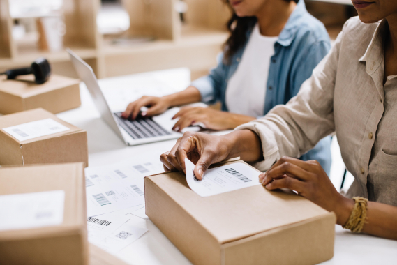 Business packing orders with a laptop in the background, managing e-commerce logistics.